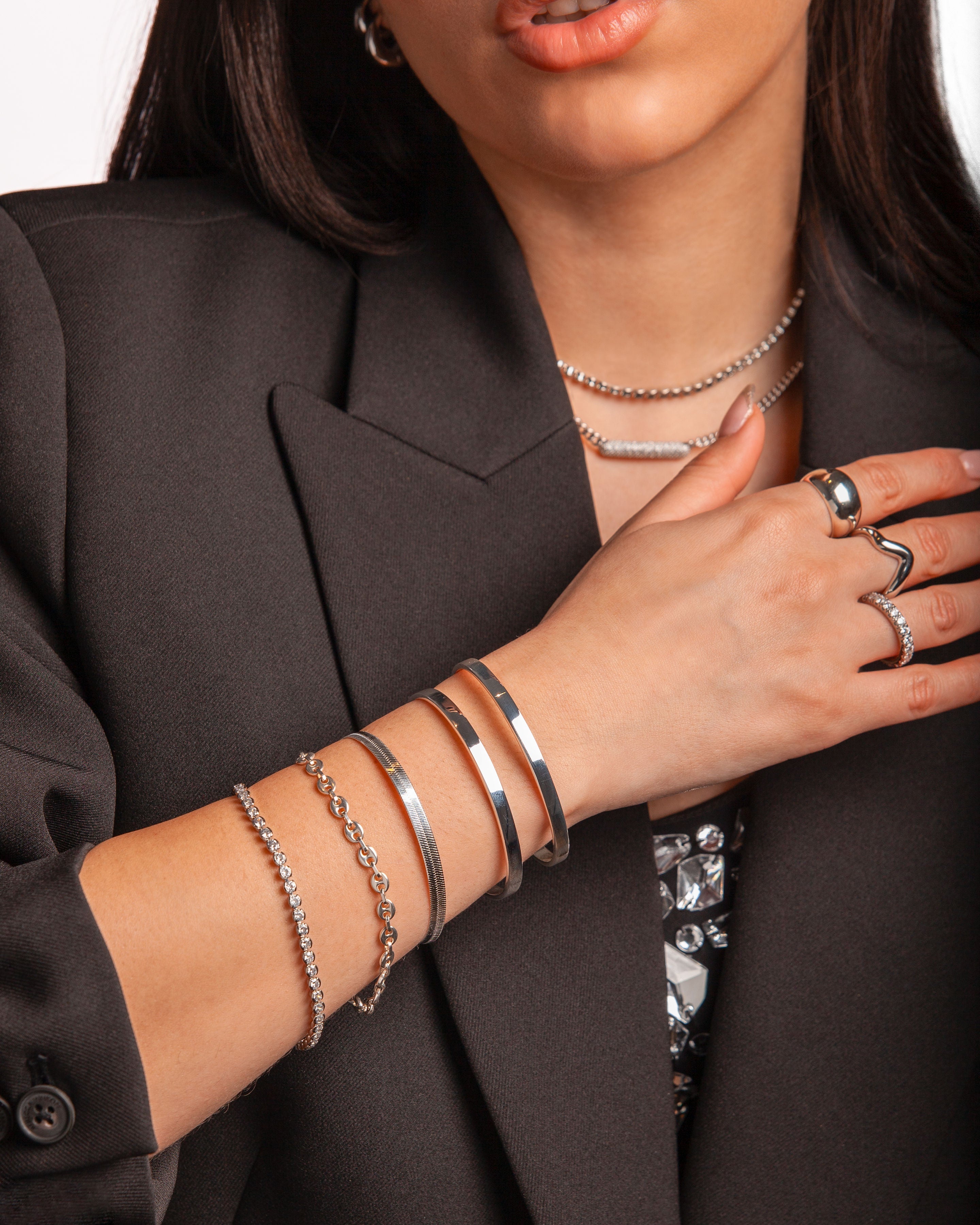 Stylish silver bangles and rings worn by a model in a black blazer, featuring elegant designs.