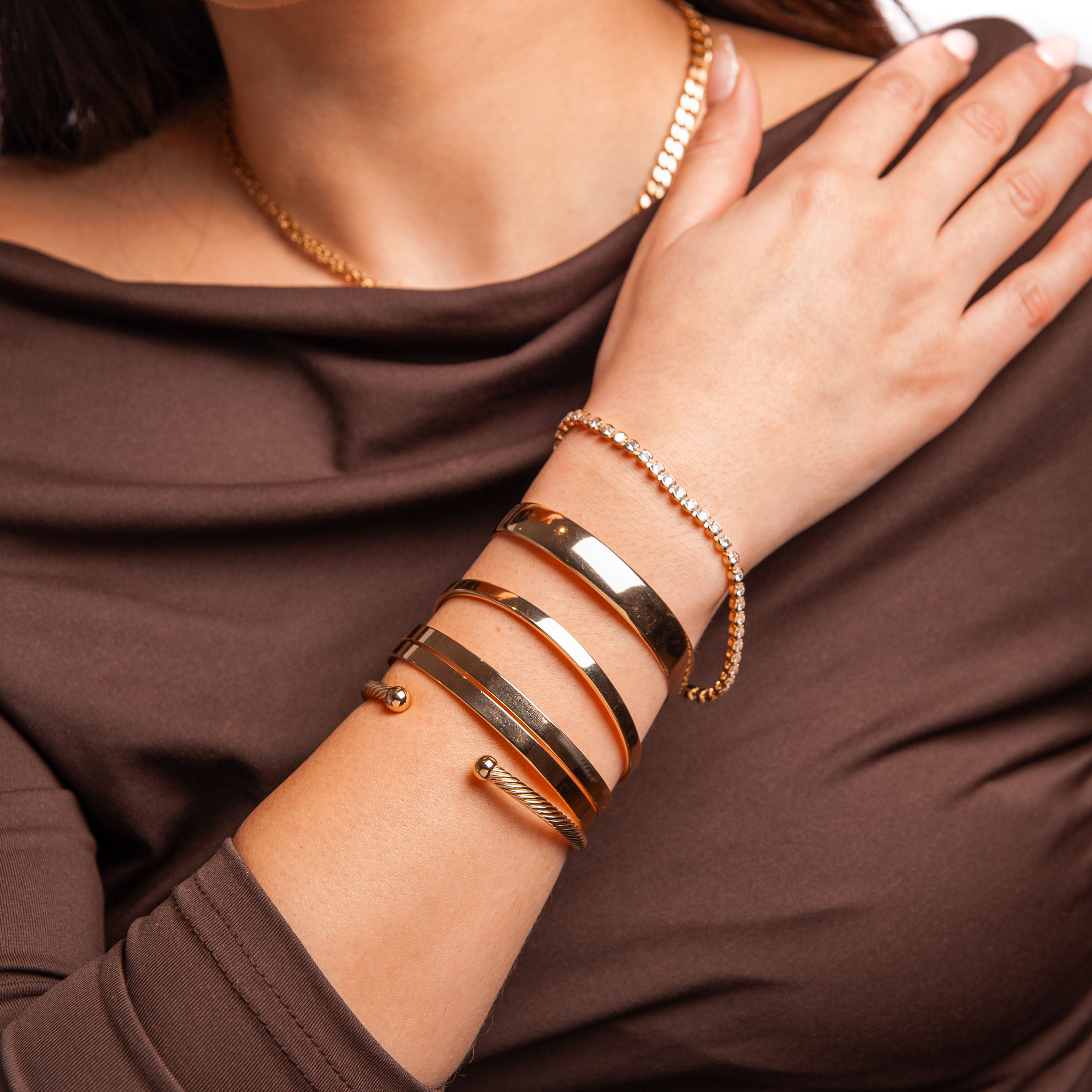 Stylish gold bangles and bracelet on a woman's wrist, featuring elegant designs and shiny finishes.
